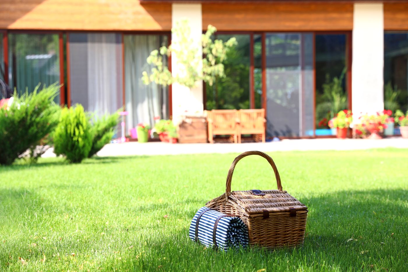 Picnic basket and striped blanket on a freshly mowed lawn in front of a house