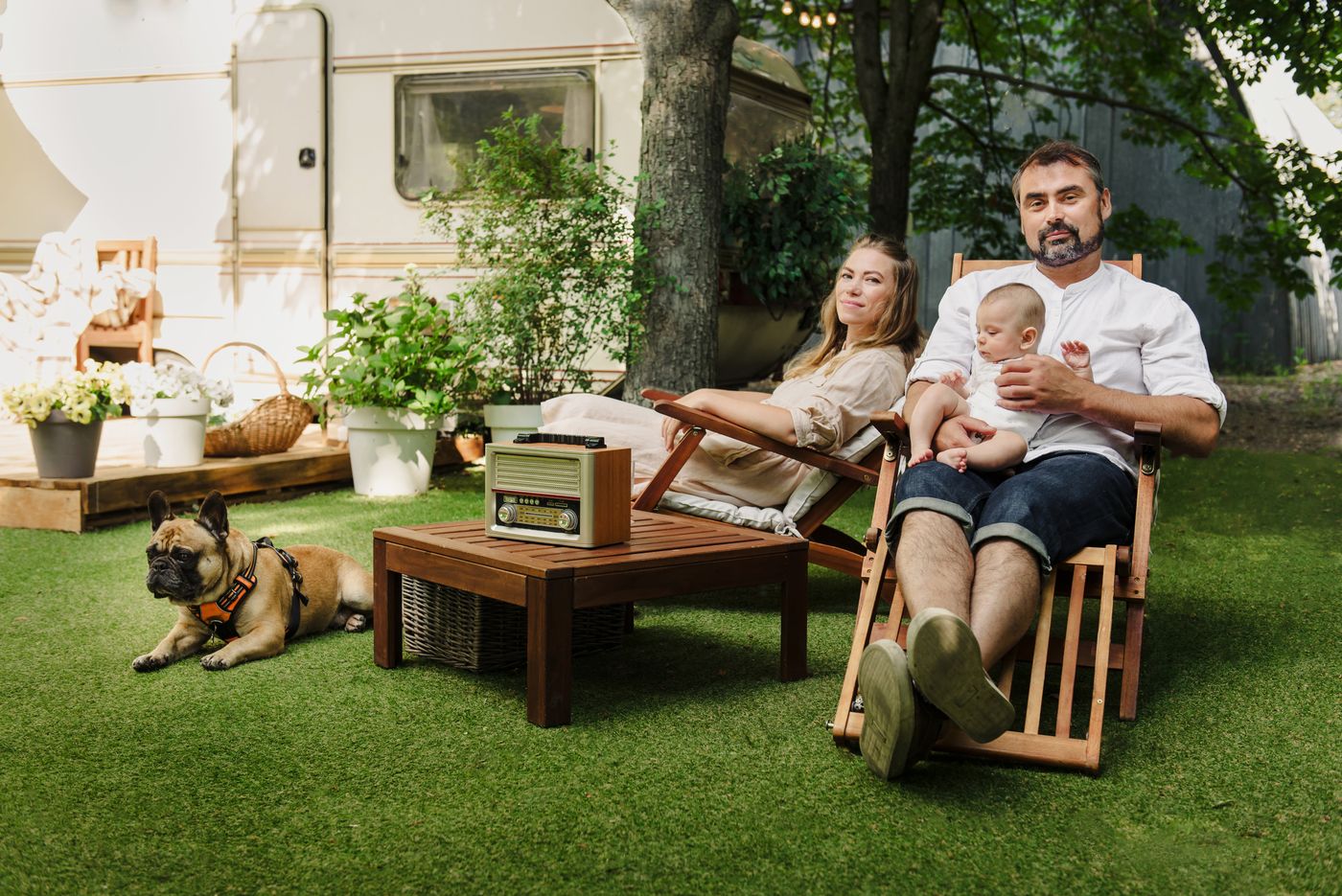 Family relaxing in wooden lawn chairs with their dog on a green lawn